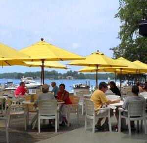 People sit at a lakeside cafe under bright yellow canapes.