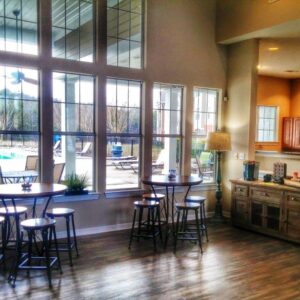 A set of small bar tables and stools line a window that overlooks a pool.