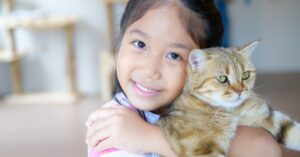 A young girl hugs a cat to her.
