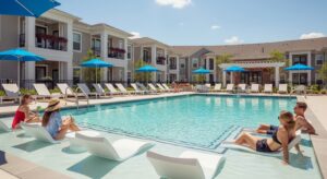 A luxurious resort-style swimming pool and sundeck at Riverwalk Apartment Homes on a bright, sunny day.