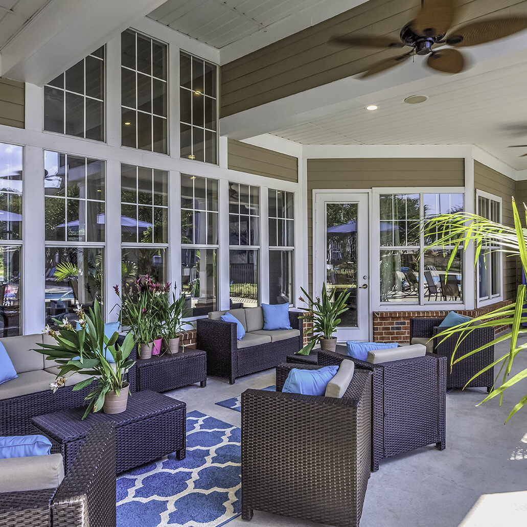 A comfortable covered patio with ceiling fans, palms, and chairs.